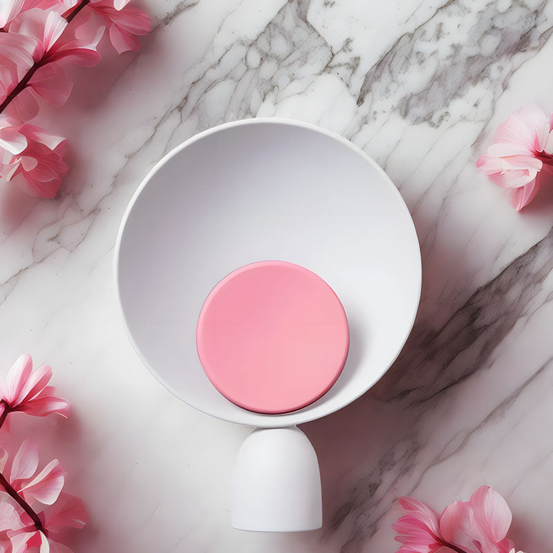 Wavello nachtlamp met een modern design, gefotografeerd van bovenaf op een marmeren oppervlak, omringd door roze bloemen. De lamp heeft een witte kegelvormige reflector en een zachte roze cirkel in het midden. Het stijlvolle en kalmerende ontwerp maakt het een perfecte aanvulling voor elke slaapkamer of woonkamer.