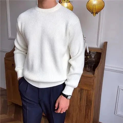Man draagt een stijlvolle, comfortabele witte Zarvo Trui met ribstructuur en ronde hals, gecombineerd met een donkere pantalon voor een moderne en elegante look.