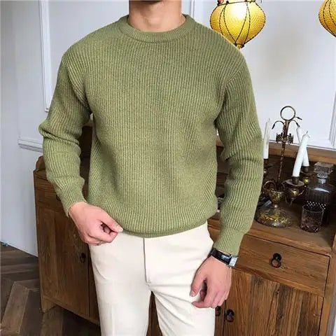 Man draagt een comfortabele, groengekleurde trui met ribstructuur en een klassieke ronde hals, gecombineerd met beige broeken. De Zarvo Trui straalt stijl en eenvoud uit, perfect voor een casual en verzorgde look.