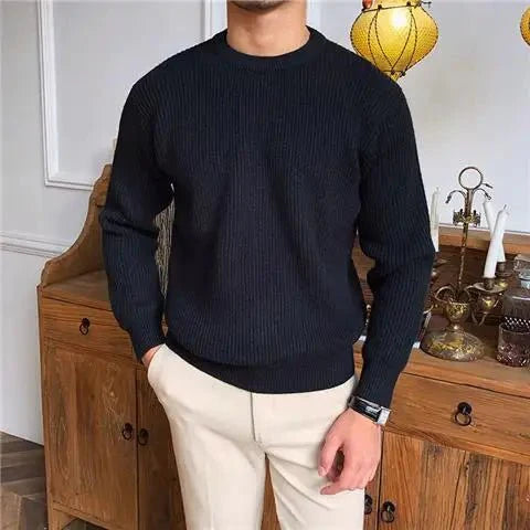 Man draagt een stijlvolle zwarte trui met een comfortabele pasvorm, gecombineerd met beige broeken. De Zarvo Trui biedt warmte en comfort, perfect voor een casual maar verfijnde look.