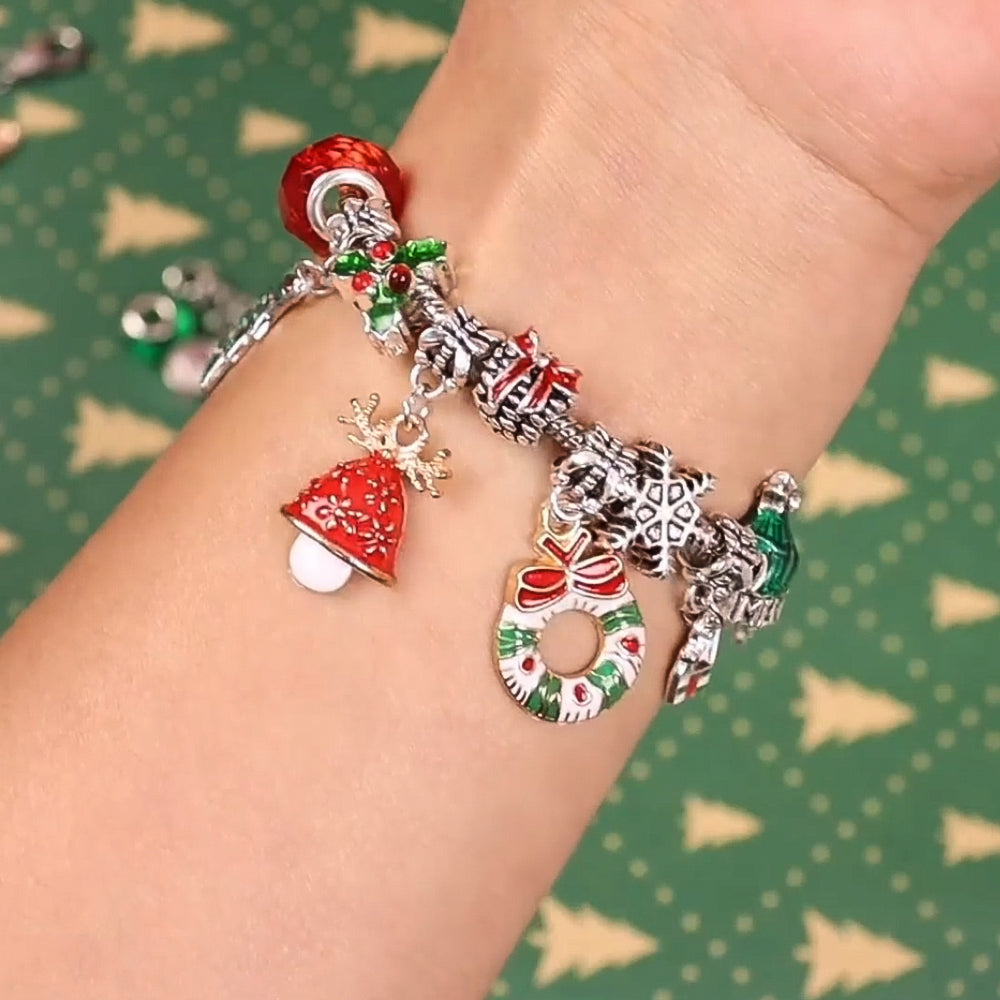 Zentoro armband met kerstthema charms, waaronder een bel, een kerstkrans, en een cadeau, gedragen om de pols, op een feestelijke groene achtergrond met kerstbomen.