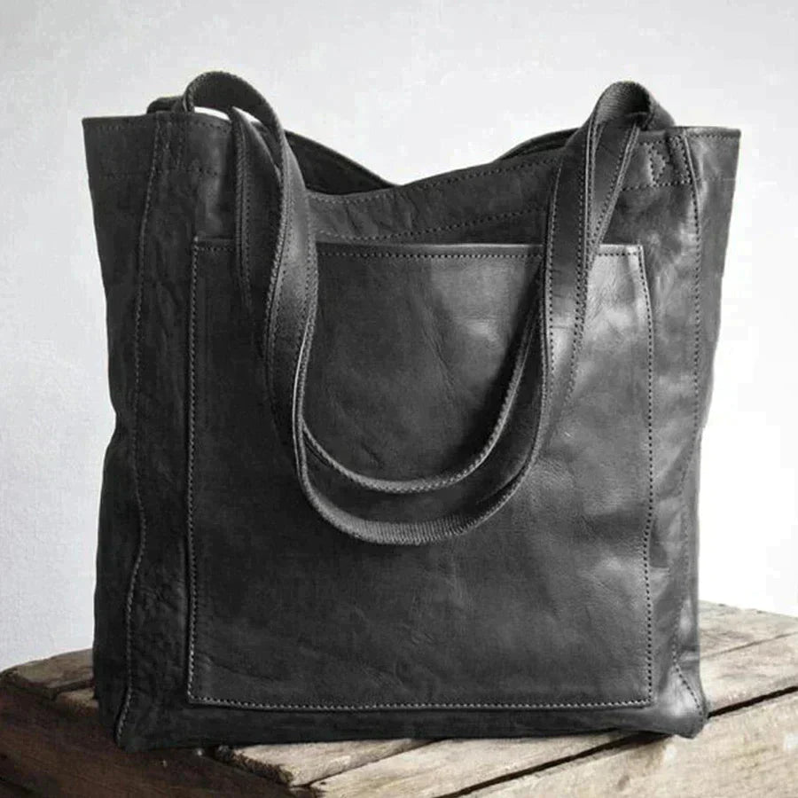 Een elegante zwarte leren schoudertas met een praktisch ontwerp. De tas heeft stevige handvatten en een ruime binnenkant, ideaal voor dagelijks gebruik en het dragen van al je spullen. De voorzak maakt het gemakkelijk om kleinere items op te bergen.