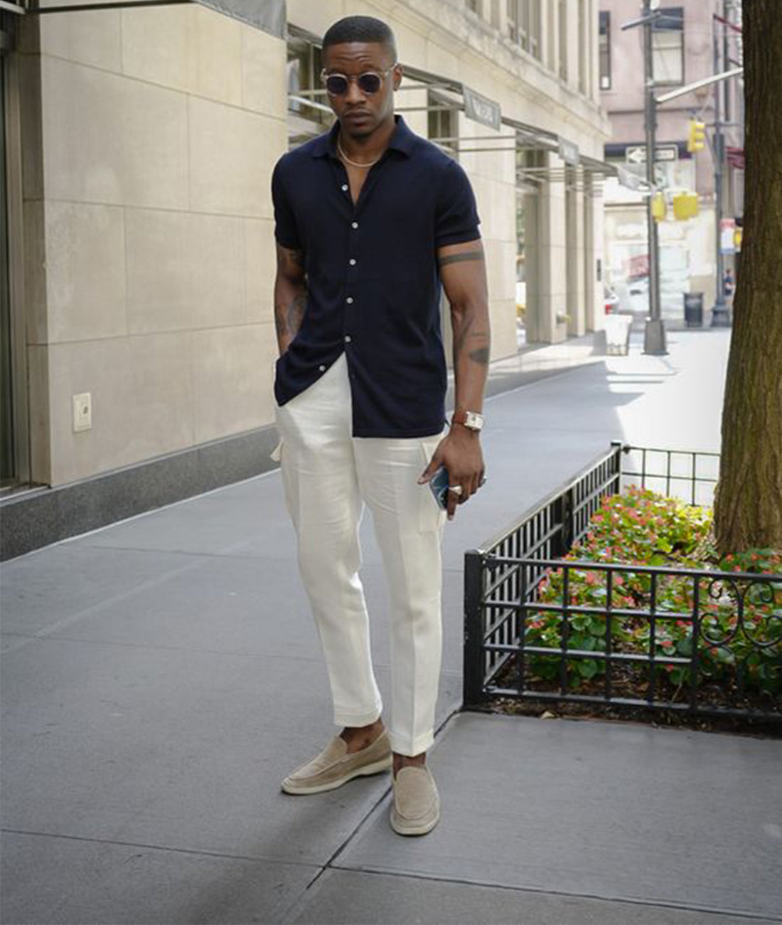 De afbeelding toont een man in een stijlvolle zomerse outfit, bestaande uit een donkerblauwe overhemd met korte mouwen en een witte broek. Hij draagt Zodara klassieke herenloafers in een beige kleur, die perfect passen bij zijn casual, maar verfijnde look. De loafers bieden zowel comfort als tijdloze elegantie, met een slanke, minimalistische uitstraling en een ademende, lichtgewicht materiaal. Deze schoenen zijn de ideale keuze voor een modieuze, zomerse stijl die zowel casual als gekleed kan zijn.