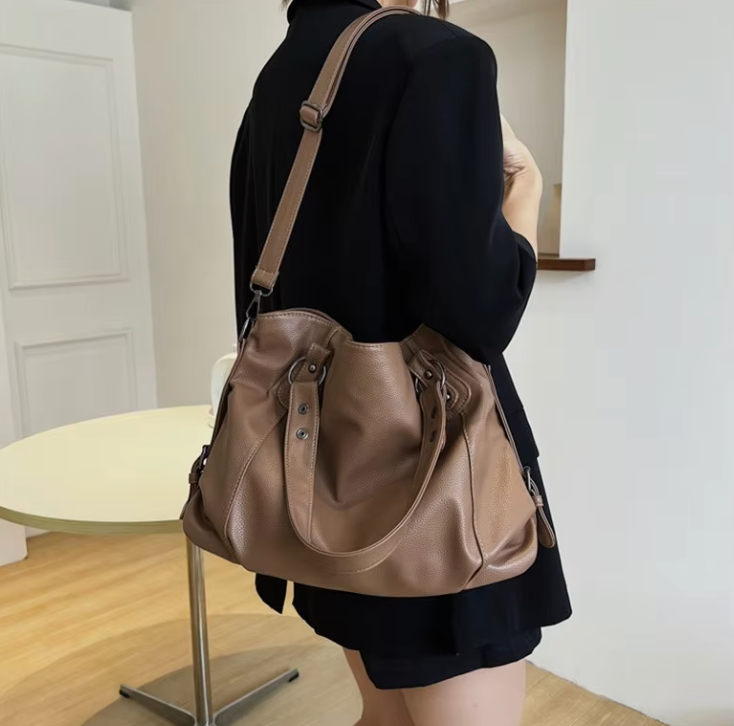 Zyrano bruine leren crossbody tas, praktisch en stijlvol, gedragen over de schouder. De tas heeft een ruim en flexibel ontwerp, ideaal voor dagelijks gebruik. De vrouw draagt de tas met een zwart jasje, wat de veelzijdigheid van het design benadrukt. De tas is afgewerkt met stevige handvatten en een verstelbare schouderriem, waardoor hij geschikt is voor verschillende gelegenheden.