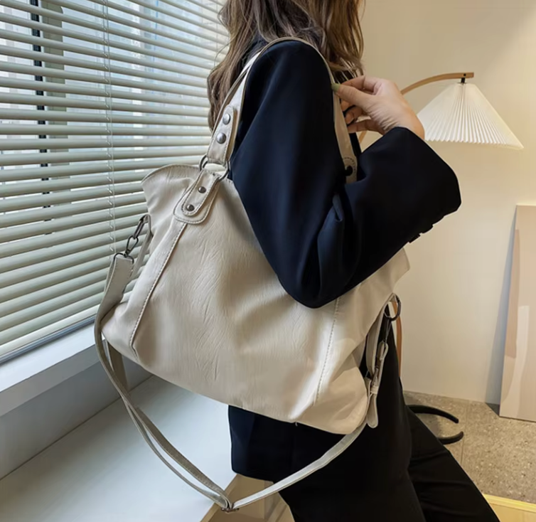 Zyrano witte leren crossbody tas, praktisch en stijlvol, gedragen over de schouder. De tas heeft een ruime, zachte structuur en wordt gedragen door een vrouw in een zwart jasje. De tas is afgewerkt met metalen accenten en een verstelbare schouderriem, wat zorgt voor zowel comfort als stijl. Het elegante ontwerp is ideaal voor dagelijks gebruik of speciale gelegenheden.