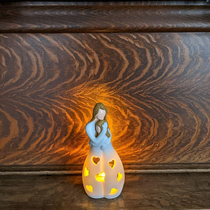 
Tijdloze kandelaar in de vorm van een moeder die haar kind vasthoudt, met hartvormige uitsparingen die een warme gloed uitstralen. De kandelaar staat tegen een houten achtergrond en creëert een sfeervol lichteffect. Perfect als decoratief item of als betekenisvol cadeau.