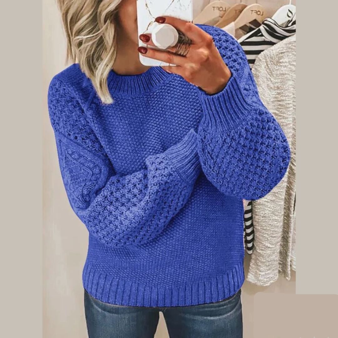 Een vrouw draagt een zachte, gebreide trui in een levendige blauwe kleur met een uniek textuurpatroon op de mouwen en schouders. De trui heeft een ronde hals en biedt zowel comfort als stijl, ideaal voor een casual look. Ze houdt een kop koffie vast terwijl ze in de spiegel kijkt.