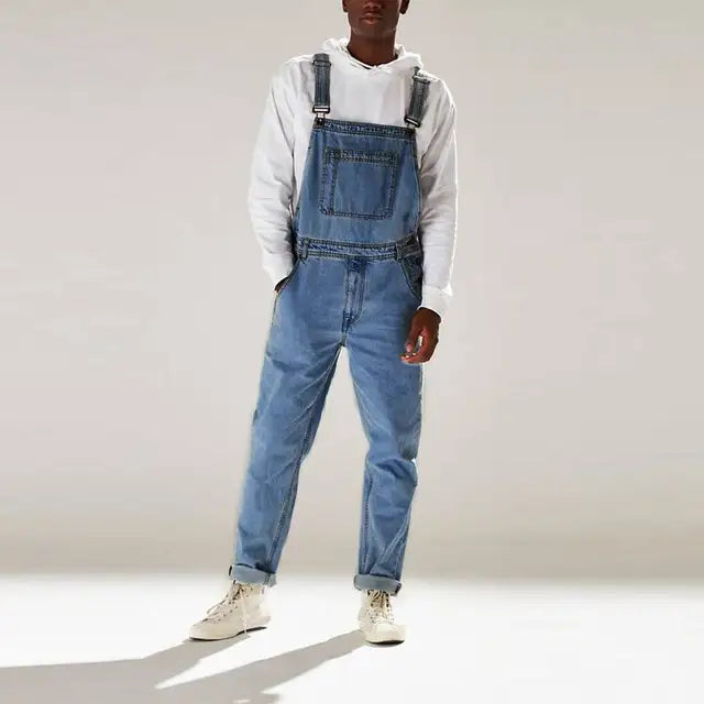 Man draagt een comfortabele denim jumpsuit met een moderne uitstraling. Het blauwe overalls is stijlvol en praktisch, met een relaxte pasvorm, ideaal voor casual zomerse looks. Het kledingstuk heeft verstelbare schouderbanden en is gecombineerd met een wit hoodie en sneakers voor een trendy en veelzijdige outfit.