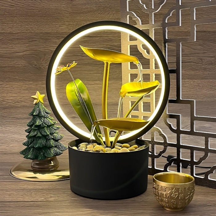 De Harmonia tafellamp, een stijlvolle combinatie van moderne verlichting en natuur geïnspireerd design, met een cirkelvormige lamp, gouden bladeren en een rustgevende waterfunctie. Perfect als decoratieve en functionele toevoeging aan elk interieur.