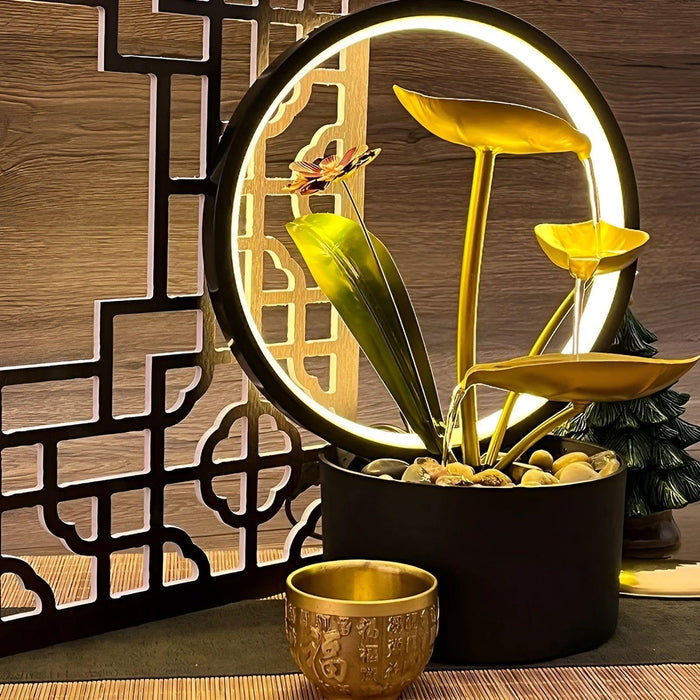 De Harmonia tafellamp, een stijlvolle en veelzijdige verlichting met een cirkelvormig ontwerp en gouden bladeren, afgewerkt met natuurlijke details zoals kiezelstenen. Deze lamp combineert elegantie en modern design, ideaal als decoratief element in elk interieur.