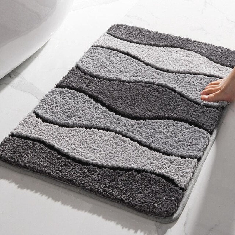 Havonia badkamer mat met een golvend design in verschillende grijstinten. De mat ligt op een marmeren vloer en een voet raakt zachtjes de rand, wat de zachte en comfortabele textuur benadrukt. Perfect voor een warme en luxe uitstraling in de badkamer.