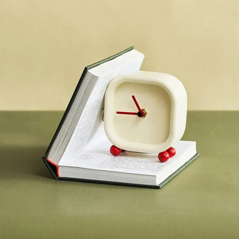 Moderne Hawley alarmklok met minimalistisch ontwerp, geplaatst tegen een open boek. De vierkante vorm en rode accenten geven een speelse en stijlvolle uitstraling. Ideaal als betrouwbare wekker of decoratief item voor je nachtkastje of bureau.