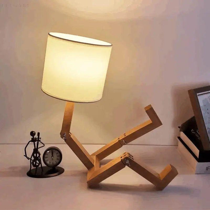 Klaarlicht tafellamp in een speelse zittende houding, gemaakt van hout met verstelbare ledematen. De lamp heeft een eenvoudige, witte kap die een warm en zacht licht verspreidt. Ideaal voor een modern en creatief interieur.