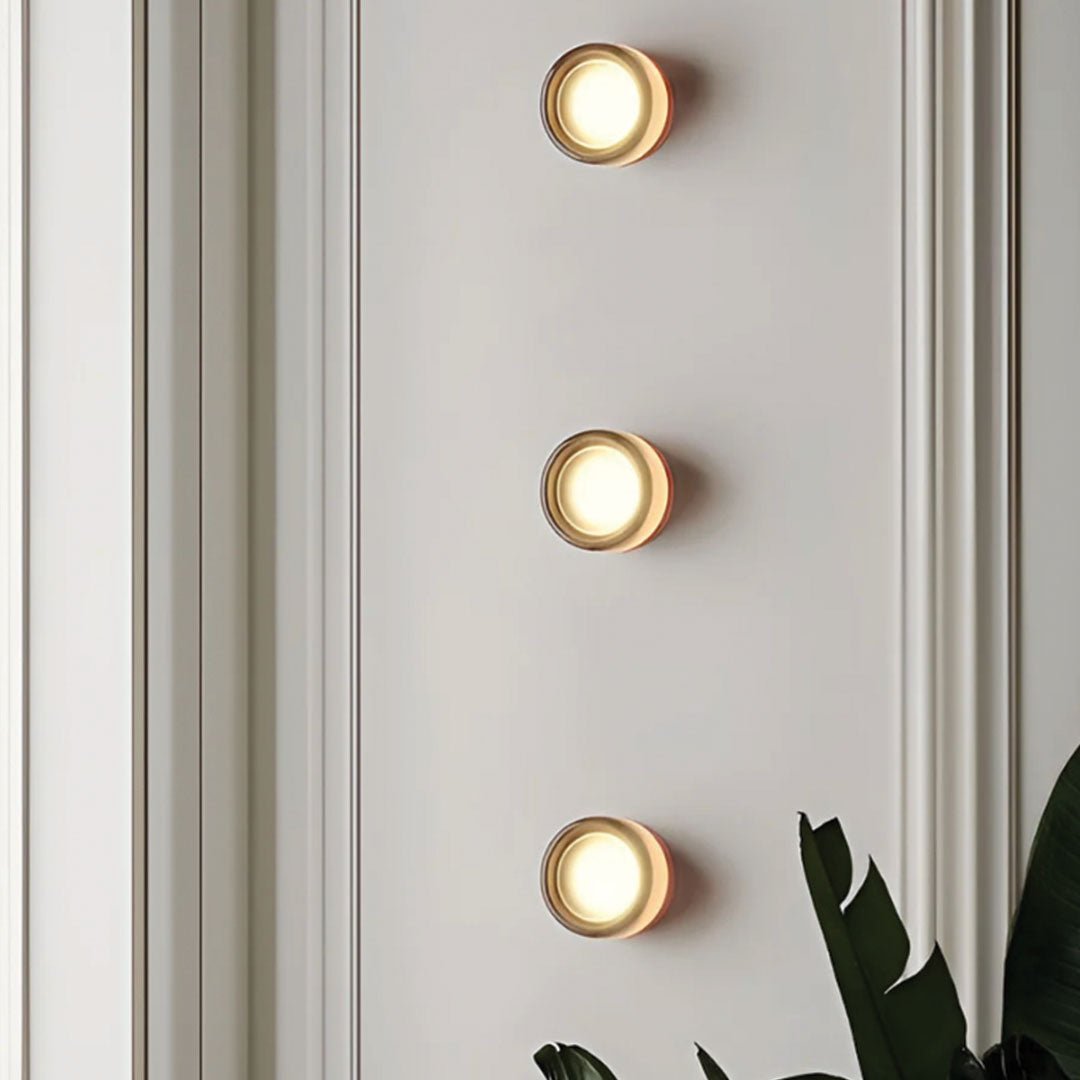 Drie stijlvolle LichtAura wandlampen in modern design, verspreiden een warme gloed op een witte muur met subtiele lambrisering, ideaal voor een eigentijds interieur.