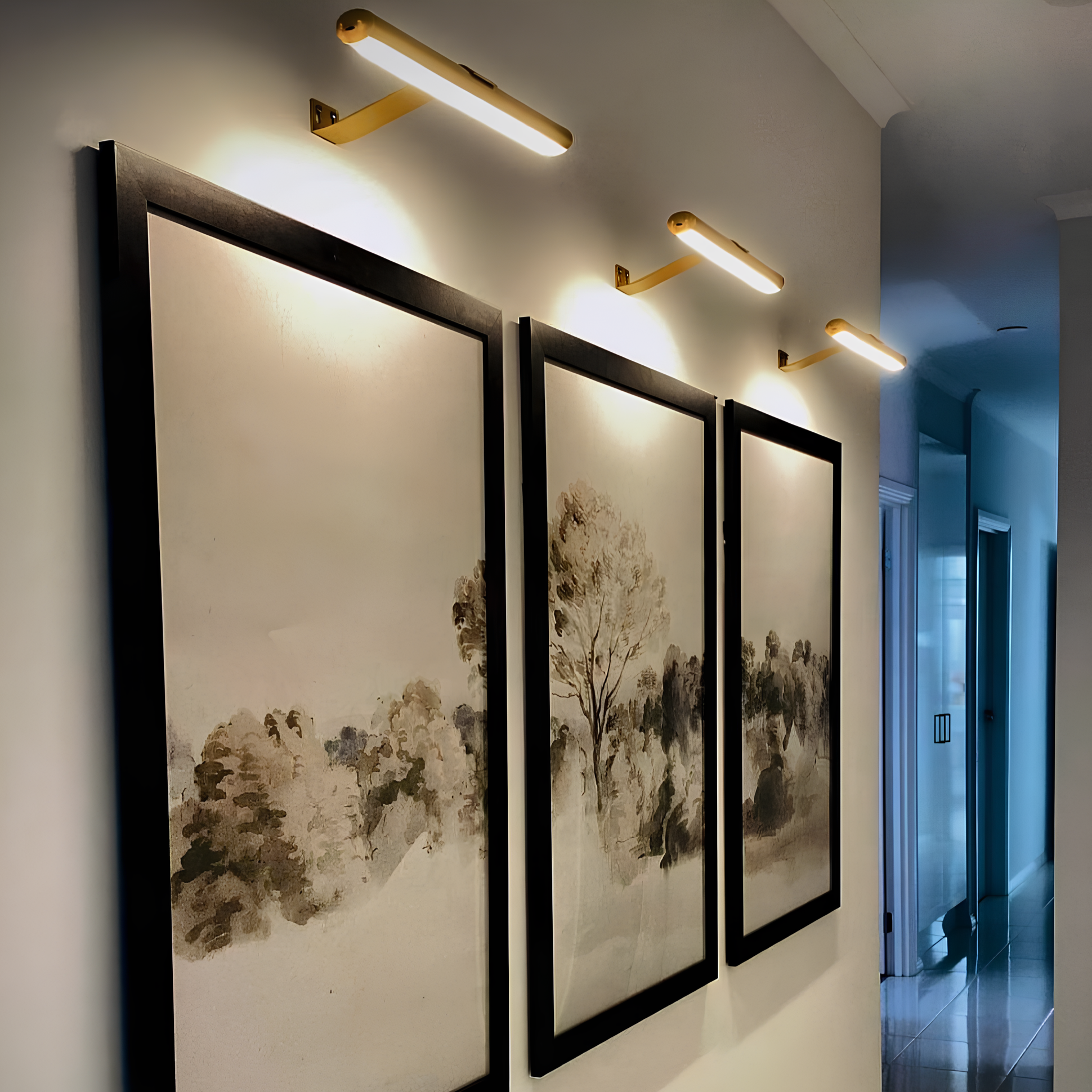 Lumenova muurverlichting verlicht kunstwerken met stijl, geplaatst boven drie ingelijste schilderijen voor een verfijnde sfeer in een moderne ruimte.