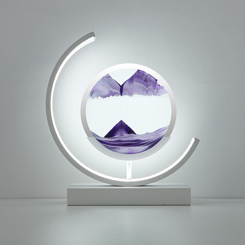 De LumiAura lamp toont een hypnotiserend landschap van paarse zandlagen die langzaam in elkaar vloeien, met een zacht omringend licht dat de levendige kleuren accentueert. Dit elegante ontwerp creëert een rustgevende sfeer in je ruimte, ideaal voor ontspanning en het toevoegen van een artistiek element aan je interieur. Het verlichte zandlandschap geeft een betoverend effect, perfect voor een kalme en moderne uitstraling.