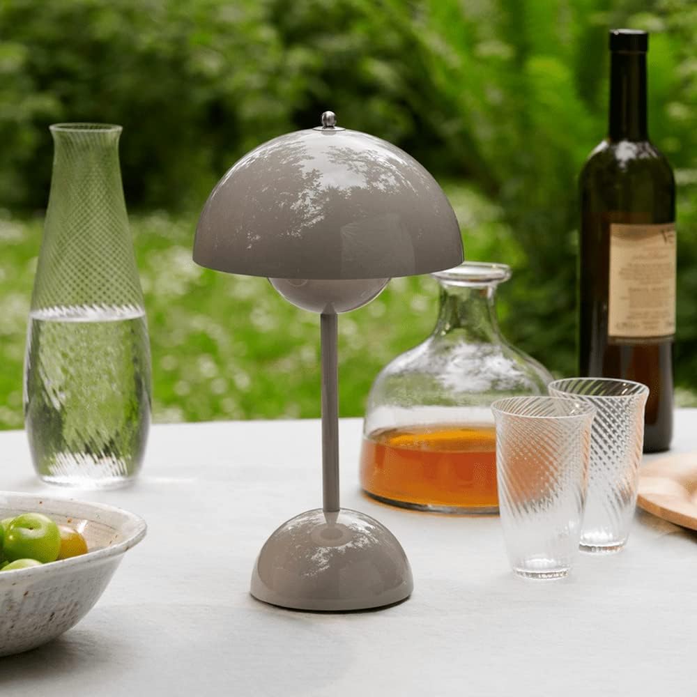 Een stijlvolle LumiNova tafellamp in grijze kleur, geplaatst op een buitentafel naast glazen drinkbekers en een karaf met drank. De lamp biedt elegante LED-verlichting en voegt een verfijnd accent toe aan de buitenruimte, ideaal voor een gezellige sfeer.