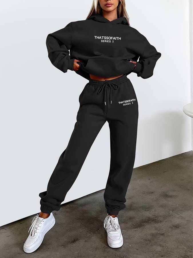 Een vrouw draagt de Nordex Jogging Set Comfortabel & Stijlvol in zwart, bestaande uit een oversized hoodie en een bijpassende joggingbroek met een elastische tailleband en trekkoord. De set heeft een minimalistisch design met een subtiel logo op zowel de hoodie als de broek. Ze combineert de outfit met witte sneakers voor een sportieve en casual look.