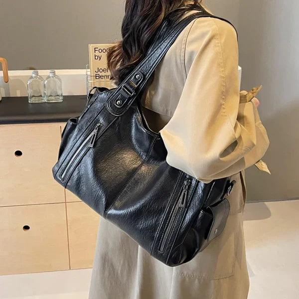 OLYNDA zwarte tote tas gedragen over de schouder met ritsvakken, gecombineerd met een beige jas, ideaal voor dagelijks gebruik en stijl.