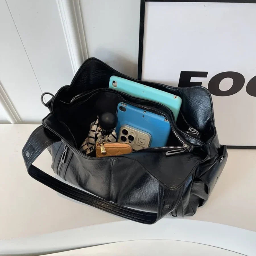 Interieur van de OLYNDA zwarte leren tote tas, met een overzicht van de inhoud, waaronder een telefoon en sleutels, perfect georganiseerd en praktisch.