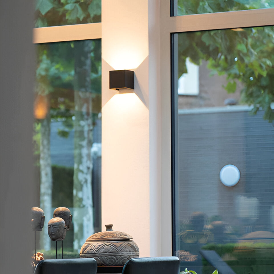 Omnira Glow verstelbare wandlamp in zwart, gemonteerd op een muur naast een groot raam, verlicht een interieurruimte met een subtiele, gespreide gloed.