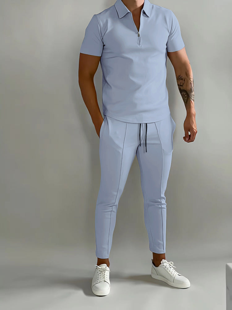 De afbeelding toont een man die een lichtblauw trainingspak draagt van het merk Opestico. Het trainingspak bestaat uit een polo met korte rits en een bijpassende broek met trekkoord, waardoor het zowel stijlvol als comfortabel is. De man combineert het met witte sneakers voor een moderne en casual look. Dit trainingspak is ideaal voor zowel sportieve activiteiten als ontspannen momenten, met een modieuze uitstraling die perfect past bij een actieve levensstijl.
