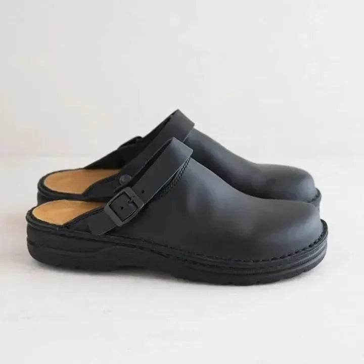 Zwarte leren orthopedische slippers met gespsluiting op een witte achtergrond.
