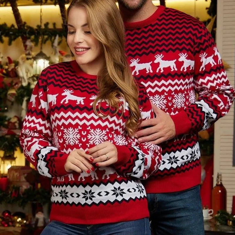 Een stel draagt matching kersttruien met een festieve rode en witte print van sneeuwvlokken en rendieren. De truien hebben een comfortabele en stijlvolle uitstraling, perfect voor de feestdagen.