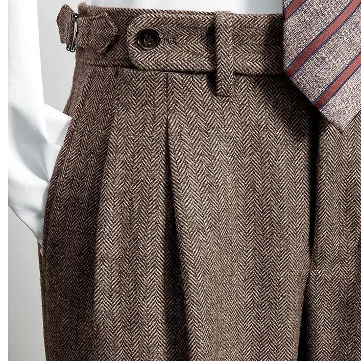 Detail van een bruine broek met een visgraatpatroon, voorzien van een riem en elegante plooien. De hoge taille zorgt voor een verfijnde en veelzijdige uitstraling, ideaal voor een chique en professionele look. Perfect voor zowel formele als casual gelegenheden.