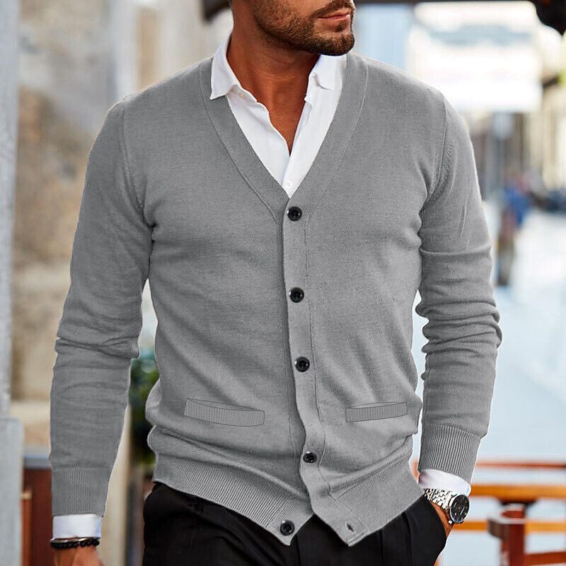 Man in een grijs casual vest met V-hals, knopen en een witte shirt eronder, wandelt door de stad. Het vest is stijlvol en veelzijdig, ideaal voor een casual of semi-formele look.