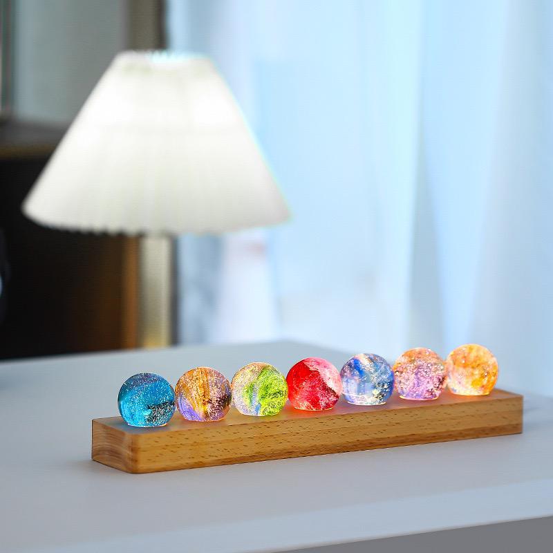 StarGlow kristallen lampen in een rij van kleurrijke bollen op een houten basis, die prachtig licht uitstralen in tinten van blauw, groen, rood, geel en oranje, en een warme, magische sfeer creëren in de kamer.