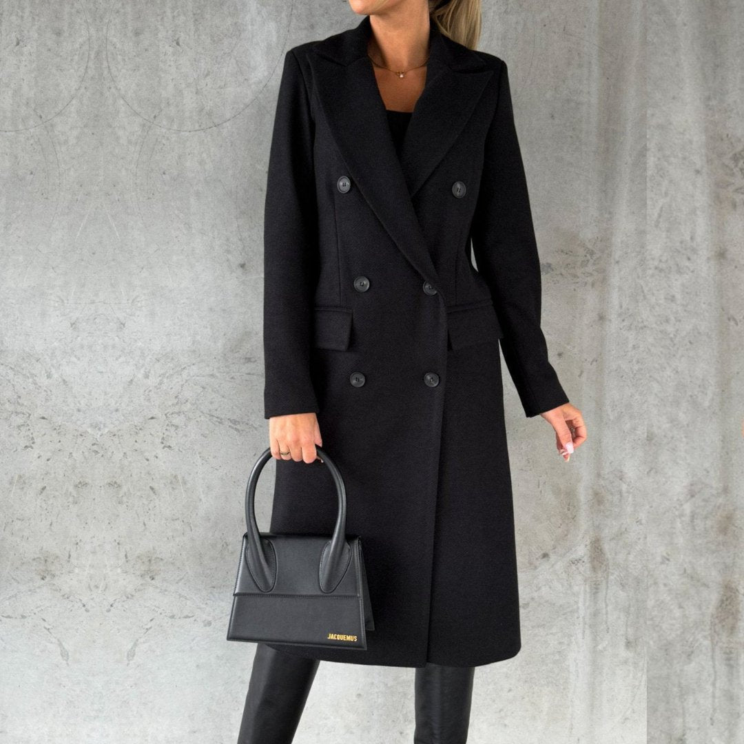 Ulara Winterjas - Een elegante zwarte lange winterjas voor dames, met een klassieke dubbele rij knopen, brede revers en praktische zakken. Gestyled met een zwarte handtas en laarzen voor een stijlvolle en functionele uitstraling.