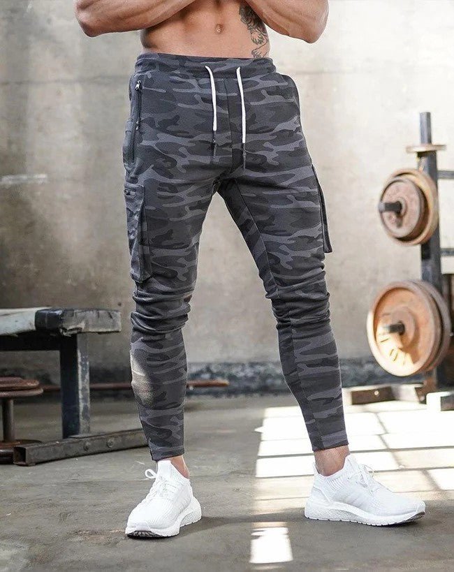 Afbeelding van de Umiro cargo jogger in camouflageprint. Deze sportieve jogger heeft een moderne slim-fit pasvorm met praktische cargozakken aan de zijkant. De elastische tailleband met trekkoord zorgt voor een comfortabele en verstelbare pasvorm. Het duurzame materiaal biedt flexibiliteit en draagcomfort, ideaal voor zowel casual als sportieve activiteiten.