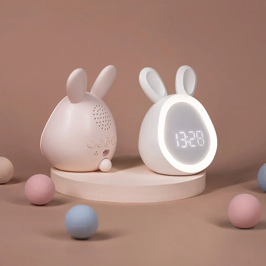 Twee Urania alarmklokken met schattig konijnontwerp, getoond vanuit verschillende hoeken. De klok heeft een LED-display en zachte verlichting, ideaal voor nachtkastjes. Achterzijde toont knoppen voor instellingen en een speaker. Perfect voor kinderen en volwassenen.