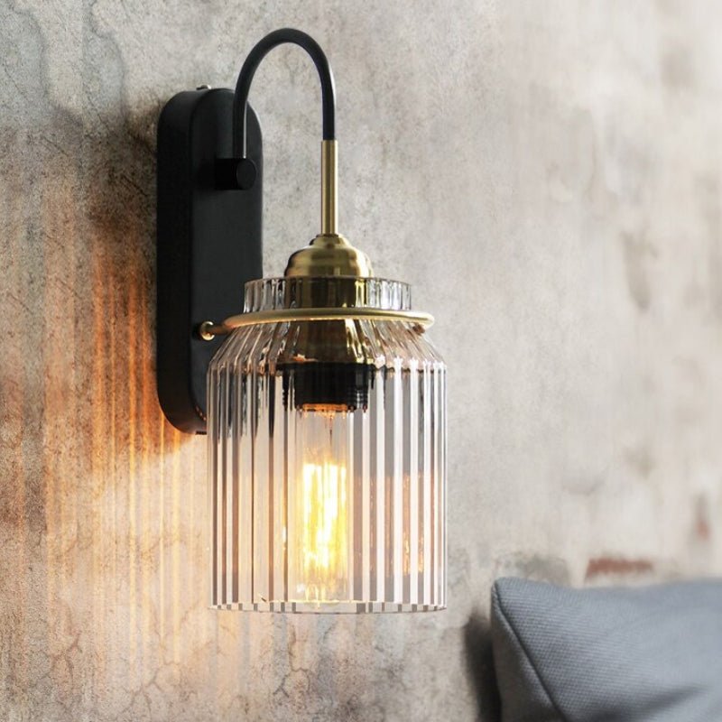 Deze wandlamp met een elegant geribbeld glazen scherm en een stijlvolle gouden afwerking voegt een vintage uitstraling toe aan elke ruimte. Het warme, zachte licht dat door het glas schijnt, creëert een gezellige sfeer, ideaal voor in je woonkamer of slaapkamer. Het ontwerp met metalen details en het klassieke glazen scherm maken deze lamp een perfecte aanvulling op je interieur.