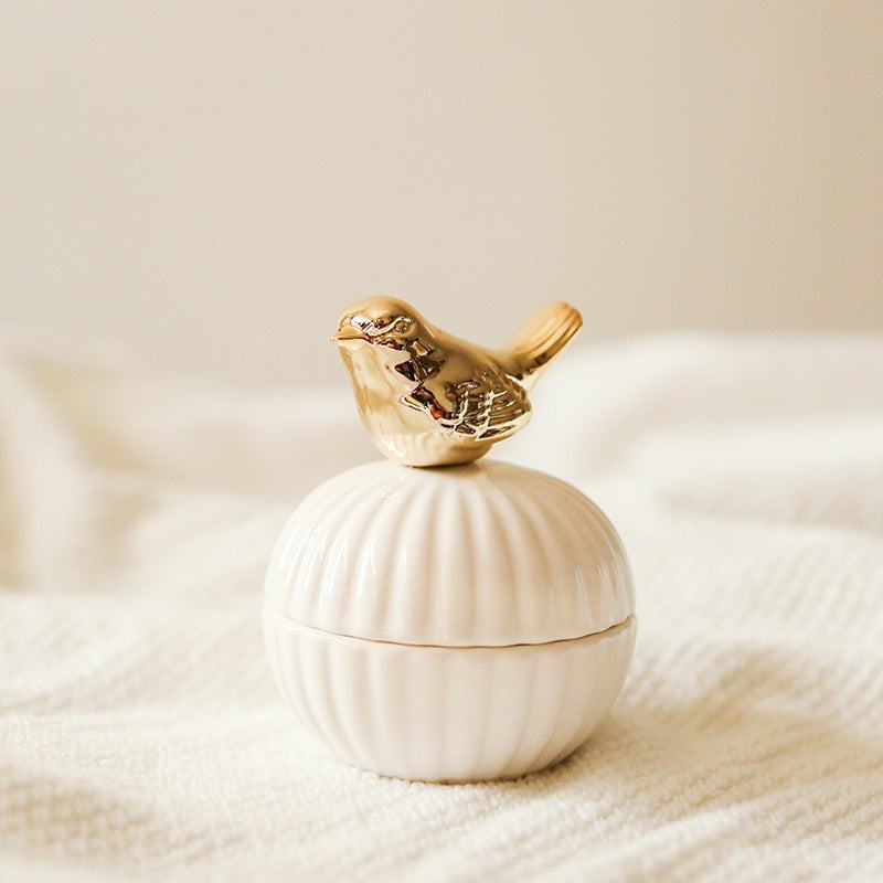 Een elegante opbergpot in de vorm van een schelp, met een gouden vogeltje als deksel. Het verfijnde ontwerp van het vogeltje en de pot voegt een charmante en verfijnde sfeer toe aan elke ruimte.