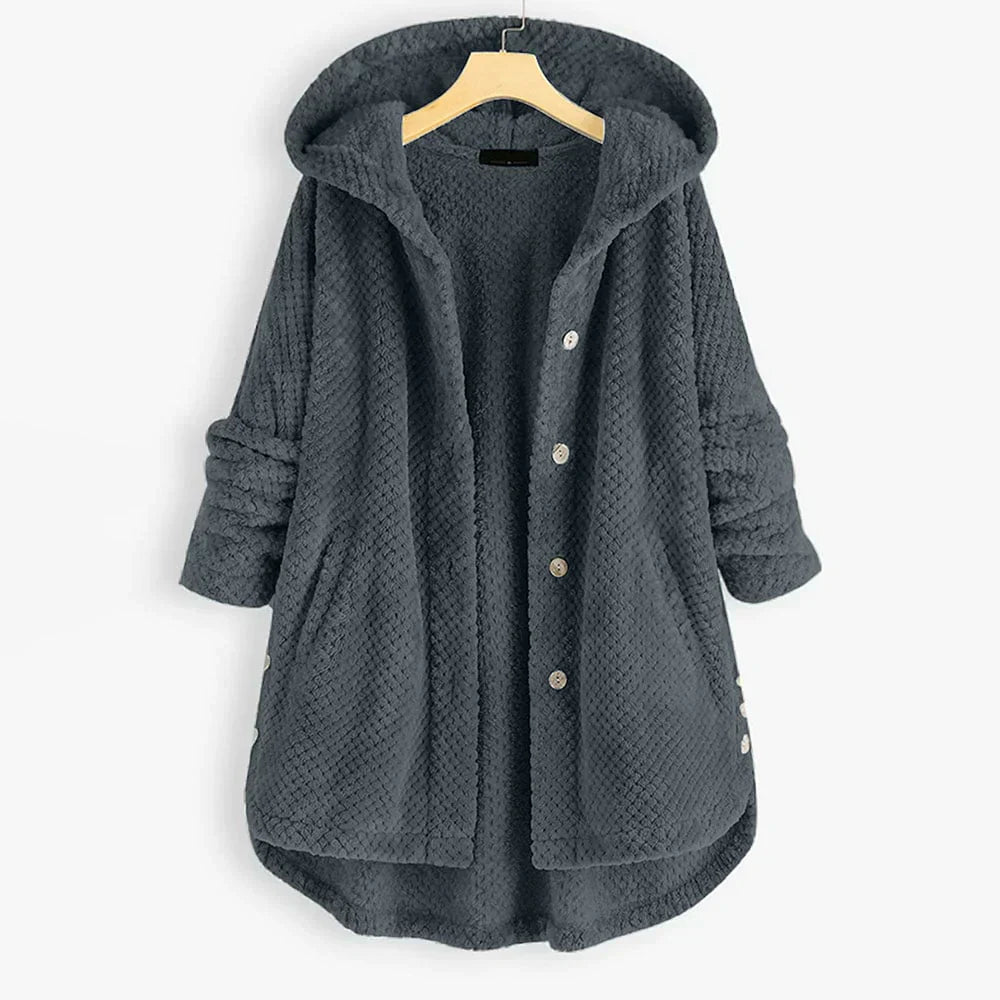 De Yara stijlvolle jas in grijs heeft een comfortabele, zachte textuur en een praktische capuchon. Deze knusse jas is ideaal voor koudere dagen, met een losse pasvorm en handige zakken aan de zijkanten. De jas is afgewerkt met knopen voor een verfijnde uitstraling, waardoor hij perfect is voor dagelijks gebruik en biedt zowel warmte als stijl.
